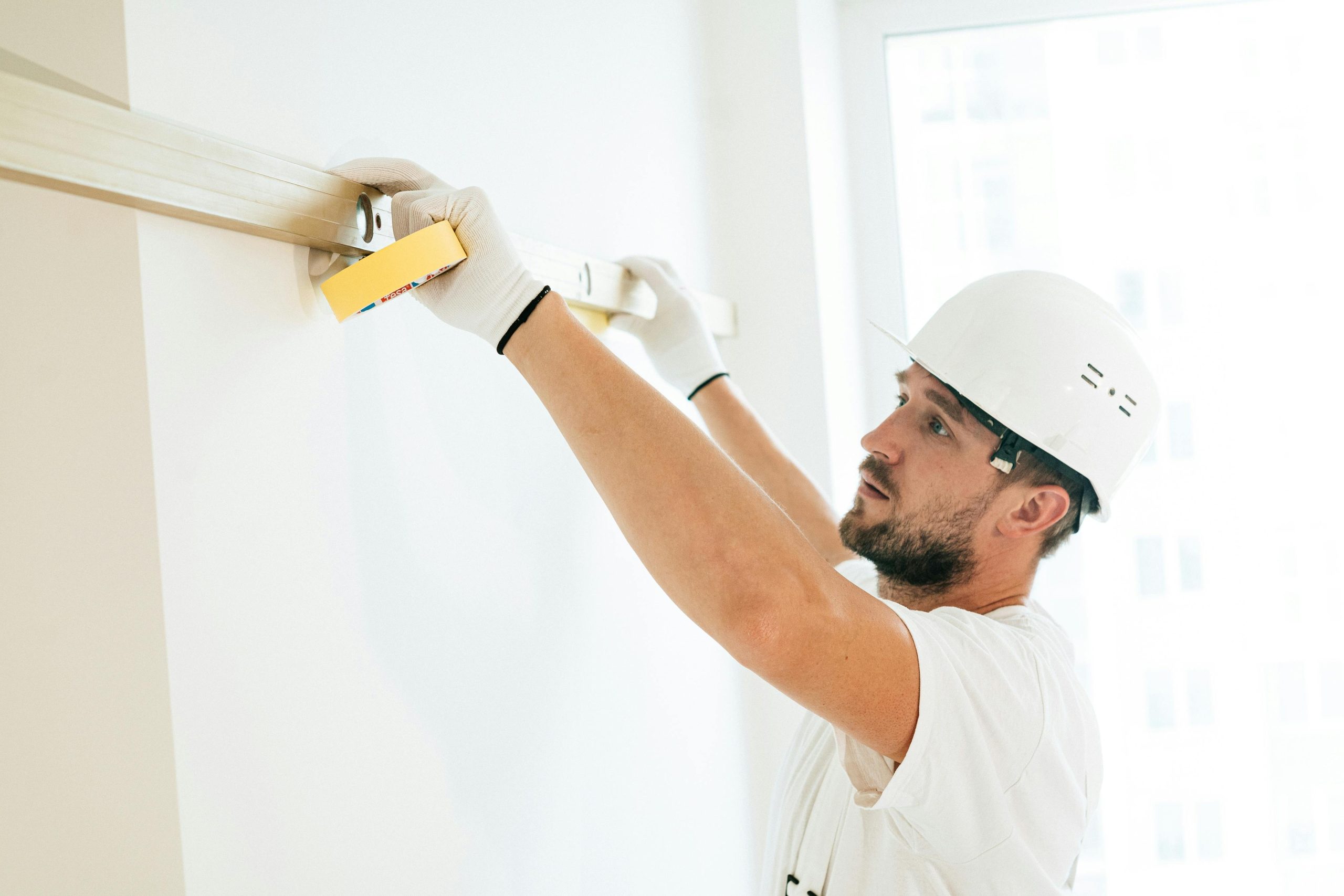 A construction worker measures a wall with a spirit level indoors.
